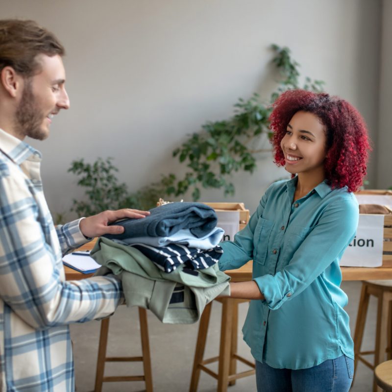 Clothing for needy. Young girl and man packing clothes to help those in need, standing in a large bright room, in a good mood.